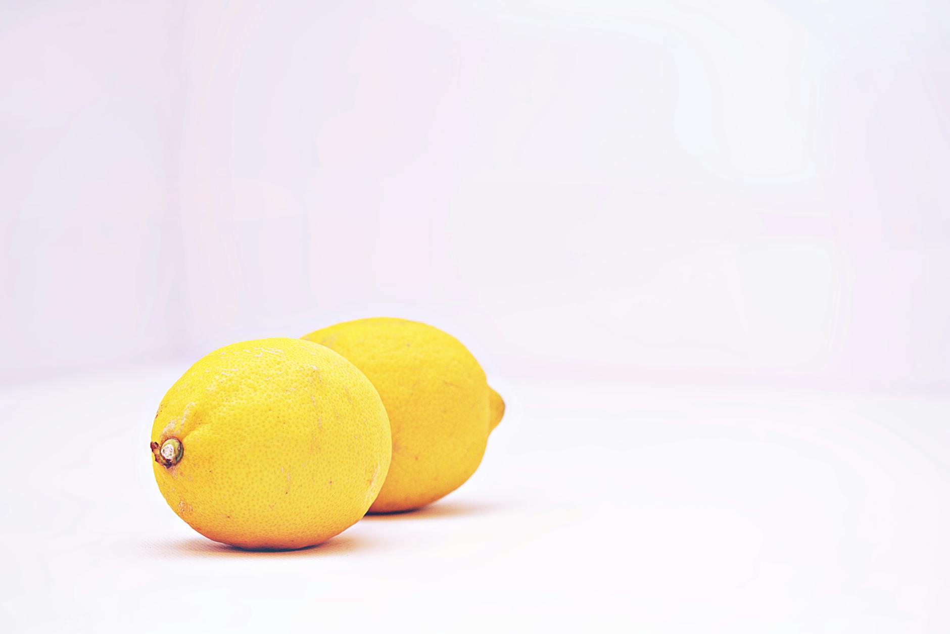 A hand holding a fresh lemon on a soft pink background