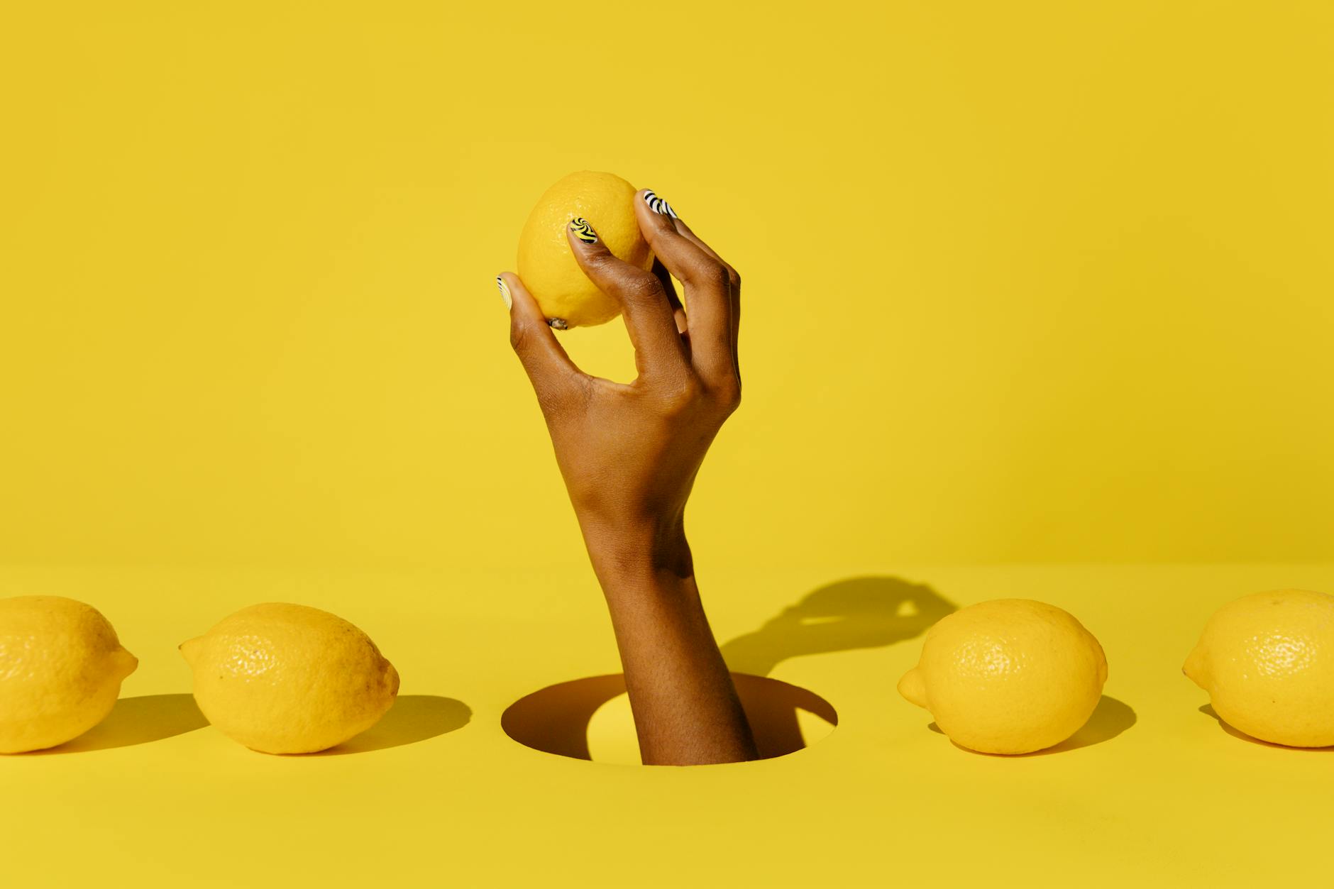 Hand holding a fresh lemon against a bright yellow background, symbolizing bright, fresh intimacy solutions