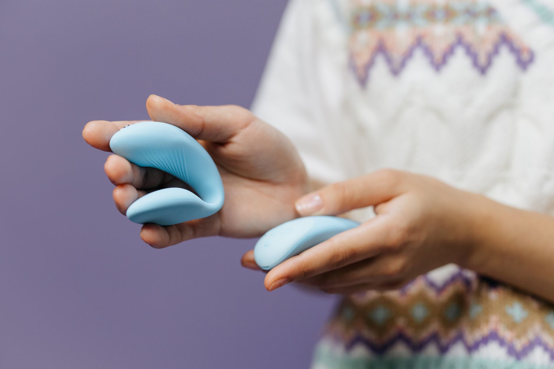 A close-up of a hand holding a lemon clitoral vibrator against a minimalistic purple backdrop.